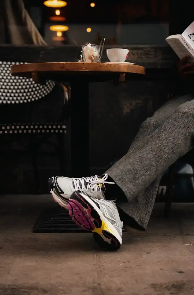 SAUCONY PROGRID OMNI 9 SS26 RELEASE An image showing a person sitting on a city street wearing Saucony ProGrid Omni 9 sneakers in a dark colorway with pink accents. (image 4 of 6)