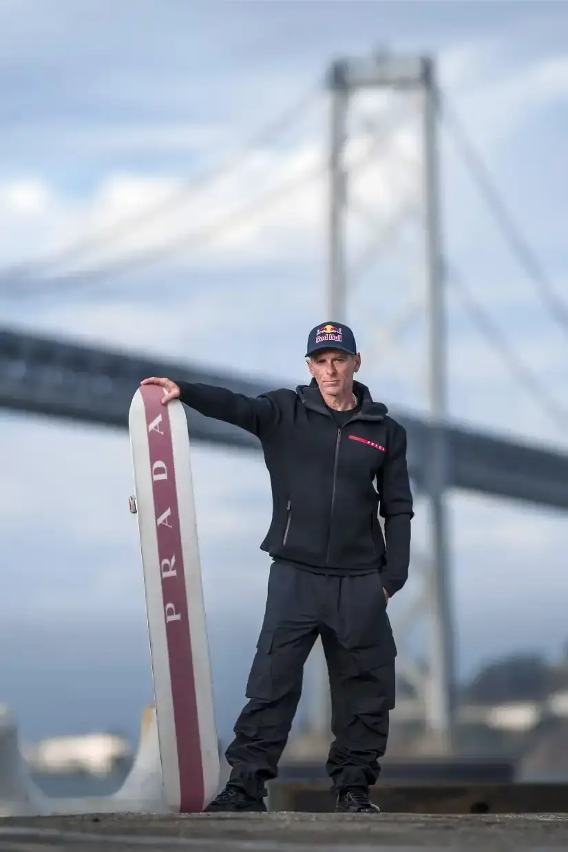 image of Professional skysurfer Sean MacCormac performs historic stunt gliding across San Francisco Bay Bridge cables after helicopter jump, supported by Prada Linea Rossa and Red Bull partnership.