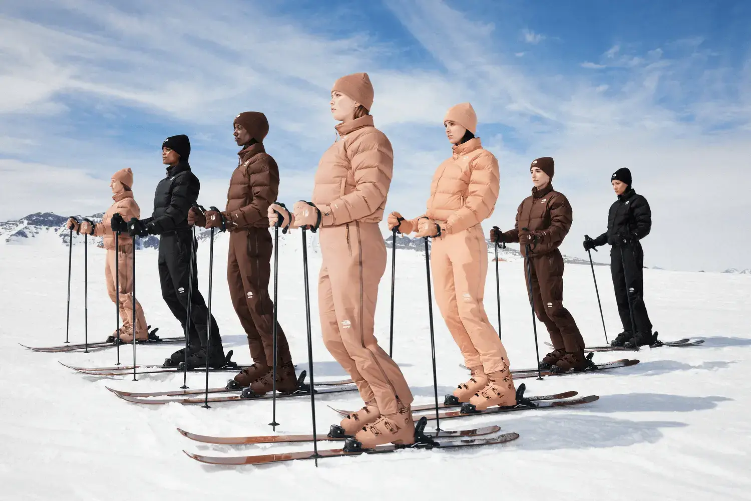Diverse group of models wearing SKIMS x The North Face collection, standing on dramatic Chilean mountain peaks, showcasing monochromatic layered winter apparel