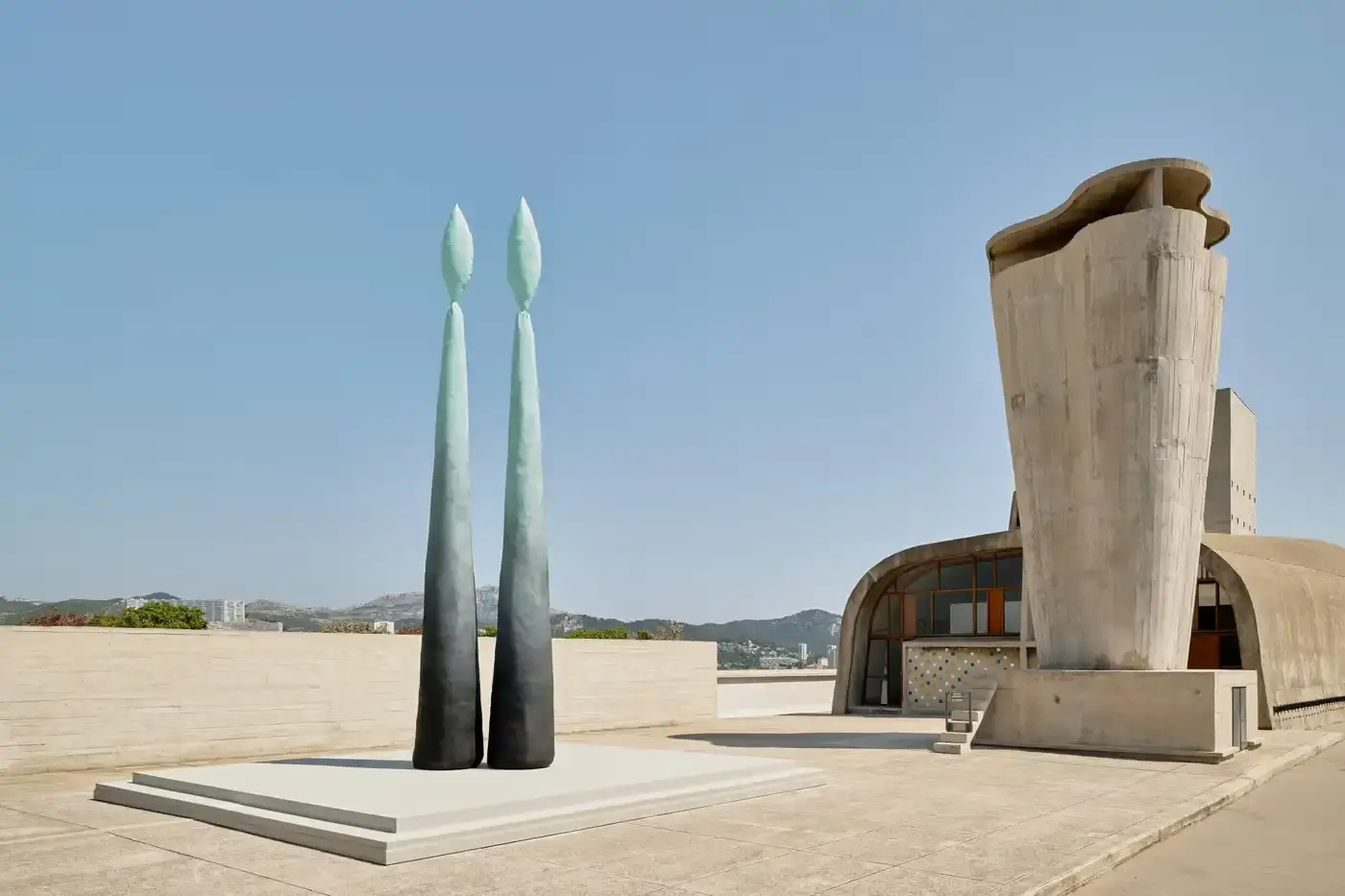 RUBY'S MATERIAL WORKS MEET LE CORBUSIER'S VISION image of American artist Sterling Ruby presents two large-scale works at MaMo by Ora Ïto in Marseille, France. The exhibition features a seven-meter bronze sculpture with green-blue patina and a seven-meter spray painting with layered color bands. Both works are displayed atop Le Corbusier's La Cité Radieuse, a UNESCO World Heritage brutalist housing complex, creating dialogue between contemporary art and historic architecture. The exhibition explores material transformation and human relationships with built environments, running through September 28, 2024. (image 3 of 5)