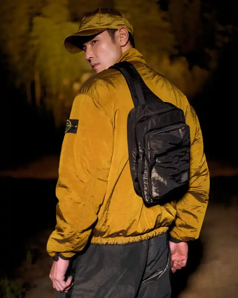 STONE ISLAND LUNAR NEW YEAR HORSE COLLECTION Stone Island introduces a Lunar New Year collection for the Year of the Horse, featuring a stand collar jacket, joggers, cap, and sling bag in NYLON METAL fabric with gold and dark brown colors. (image 6 of 10)