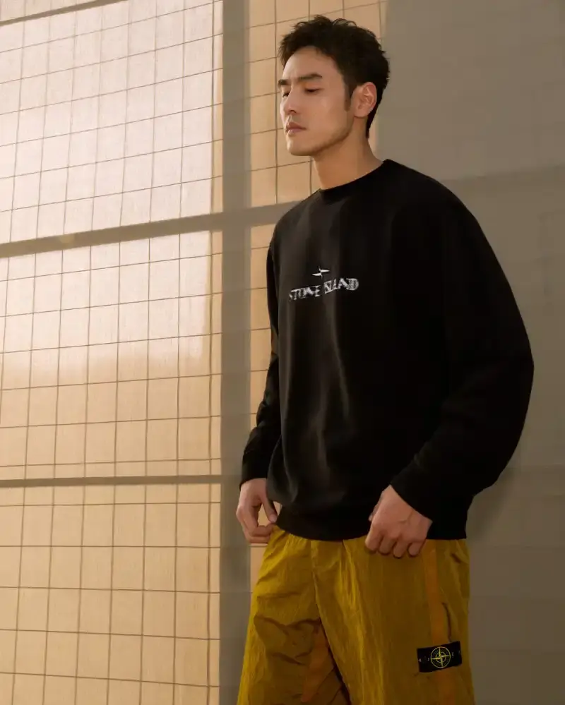 STONE ISLAND LUNAR NEW YEAR HORSE COLLECTION Stone Island introduces a Lunar New Year collection for the Year of the Horse, featuring a stand collar jacket, joggers, cap, and sling bag in NYLON METAL fabric with gold and dark brown colors. (image 10 of 10)