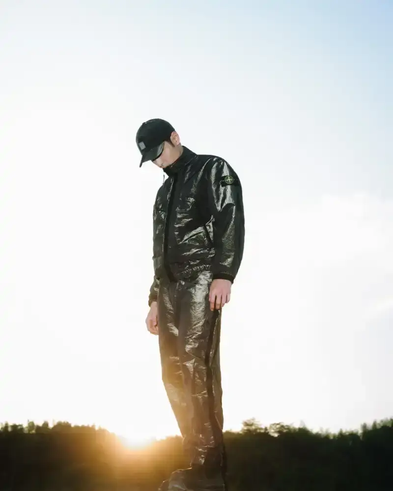 STONE ISLAND LUNAR NEW YEAR HORSE COLLECTION Stone Island introduces a Lunar New Year collection for the Year of the Horse, featuring a stand collar jacket, joggers, cap, and sling bag in NYLON METAL fabric with gold and dark brown colors. (image 2 of 10)