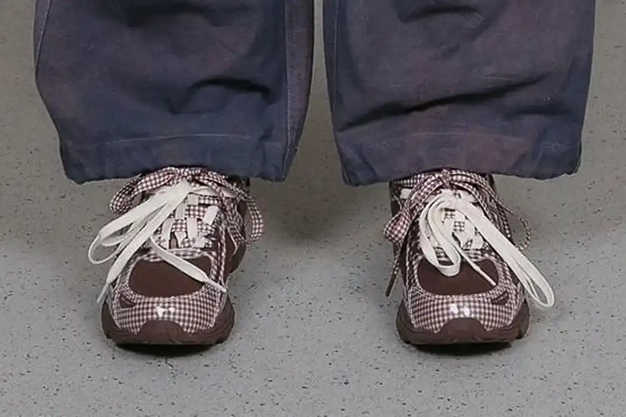 ASICS GEL-VENTURE 6 GETS GINGHAM MAKEOVER FROM STORY MFG. photo of the collaboration between sustainable fashion brand STORY mfg. and ASICS on the GEL-VENTURE 6 sneaker. It details the two gingham colorways ("Reddish Brown" and "Vanilla Violet Quartz"), the unique woven lacing system inspired by Baghdad skaters, and pricing ($133 USD). The article also describes the two-day launch event at The Truman Brewery in London on April 18-19, where visitors can contribute embroidery to a community art project while enjoying refreshments. The article provides purchase information and explains STORY mfg.'s sustainable fashion background. (image 4 of 14)