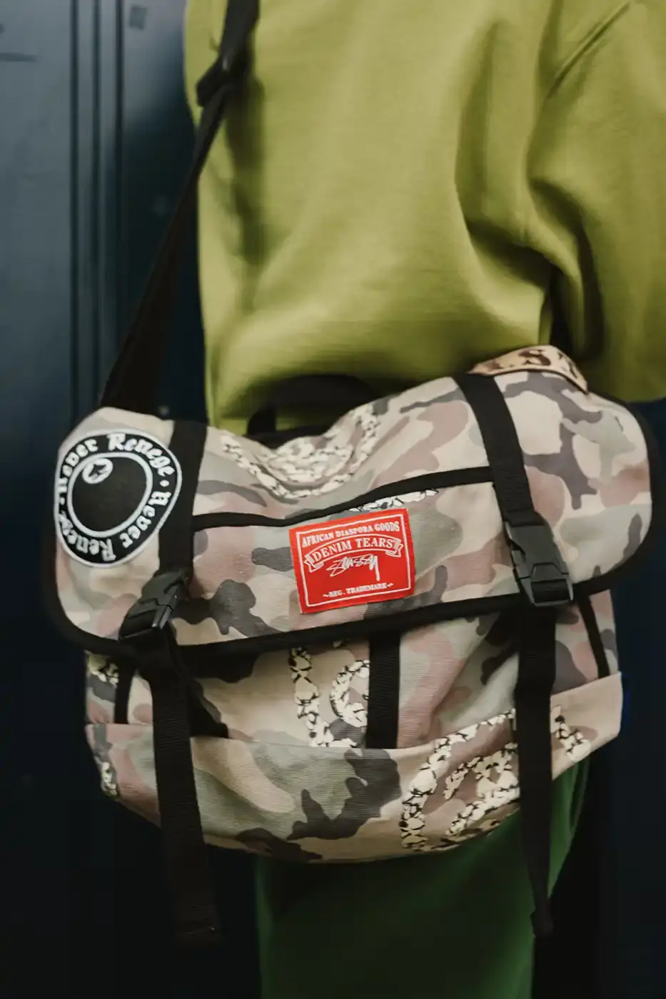 Stüssy/Denim Tears A display of Stüssy x Denim Tears' school-inspired collection, showing oxford shirts, blazers, and chinos arranged on a neutral background. The pieces feature co-branded designs and Pan-African American flag motifs. (image 9 of 11)