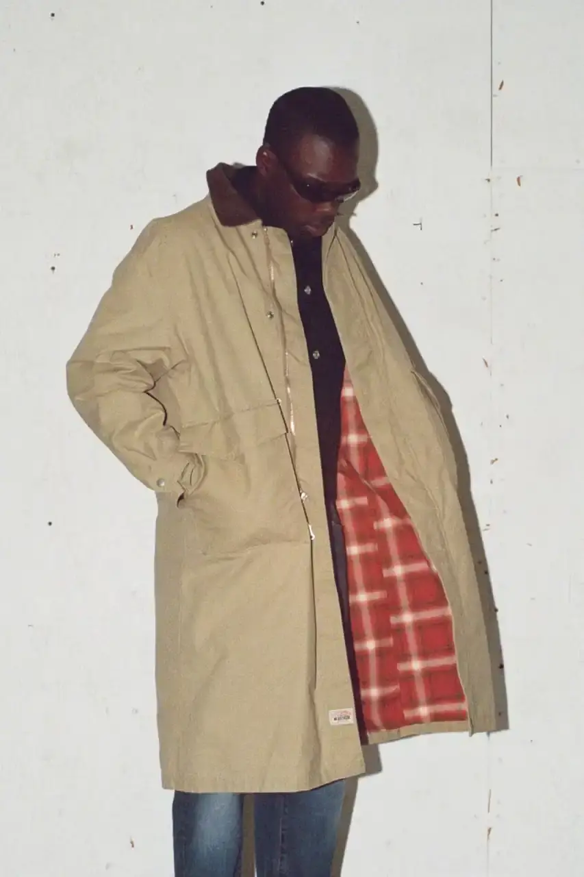 Antosh Cimoszko Stüssy Spring 2025 collection lookbook featuring an urban model wearing an oversized camouflage jacket, baggy denim trousers, and wide-cut shorts in muted green and blue tones. (image 21 of 26)