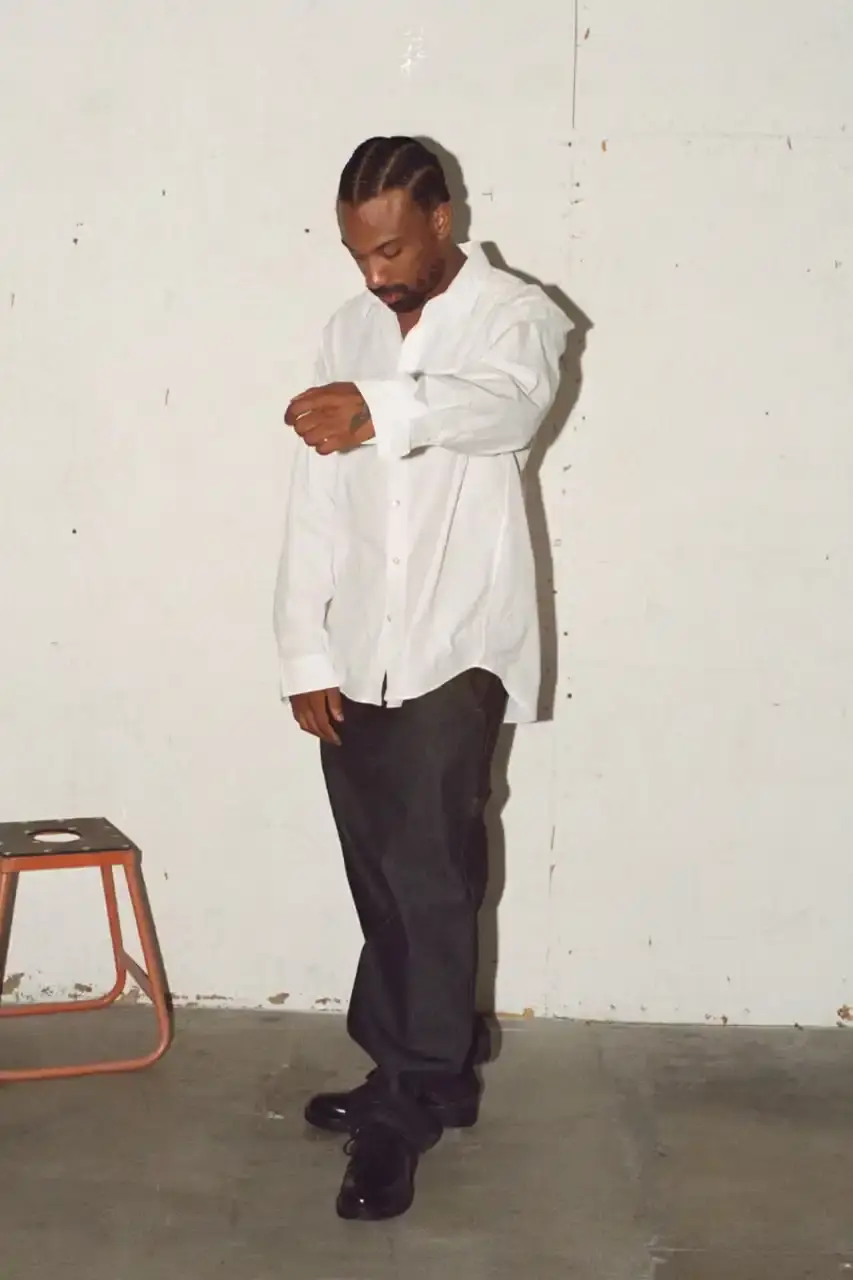 Antosh Cimoszko Stüssy Spring 2025 collection lookbook featuring an urban model wearing an oversized camouflage jacket, baggy denim trousers, and wide-cut shorts in muted green and blue tones. (image 25 of 26)