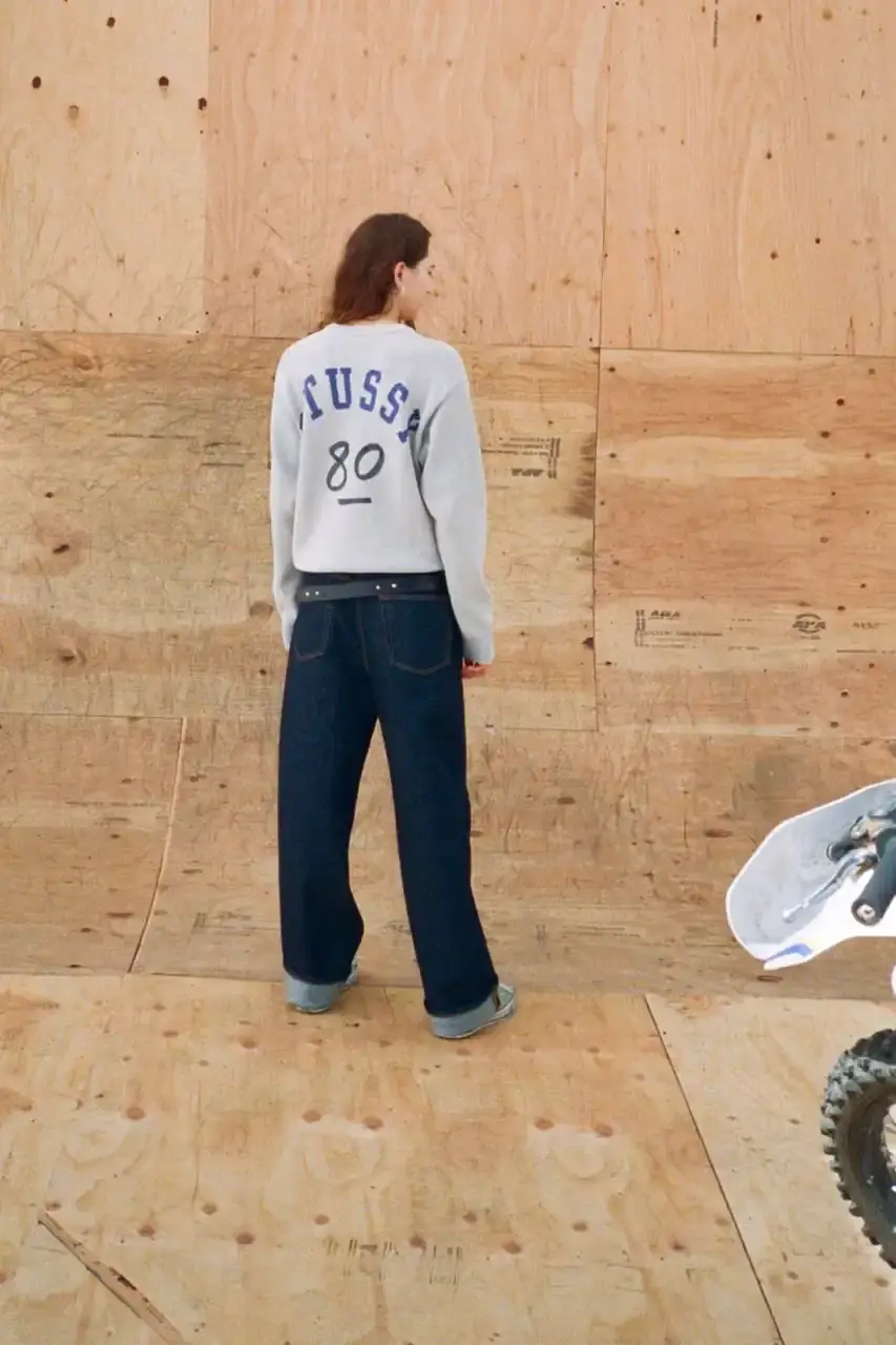 Antosh Cimoszko Stüssy Spring 2025 collection lookbook featuring an urban model wearing an oversized camouflage jacket, baggy denim trousers, and wide-cut shorts in muted green and blue tones. (image 14 of 26)