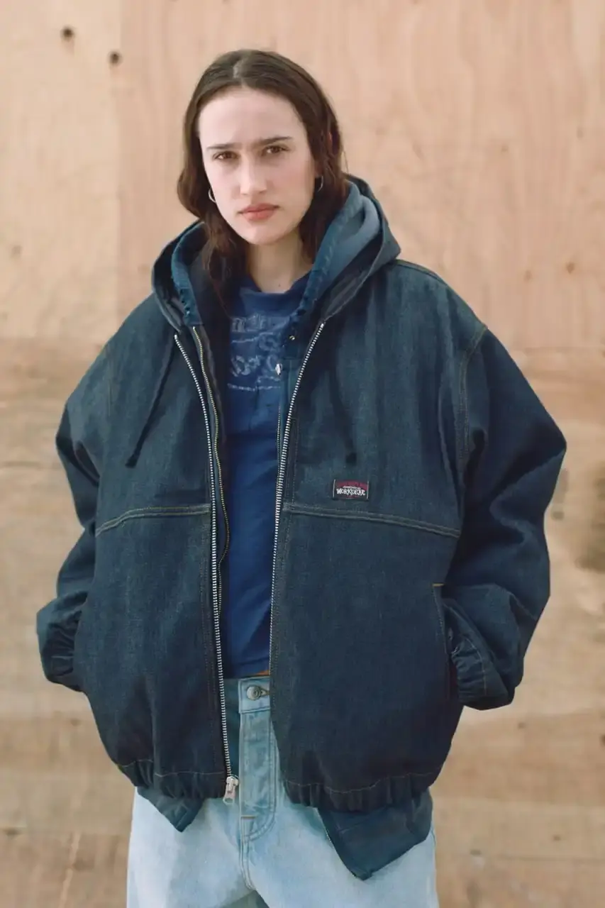Antosh Cimoszko Stüssy Spring 2025 collection lookbook featuring an urban model wearing an oversized camouflage jacket, baggy denim trousers, and wide-cut shorts in muted green and blue tones. (image 8 of 26)