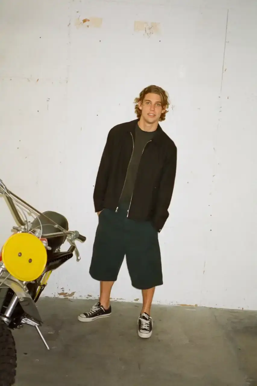Antosh Cimoszko Stüssy Spring 2025 collection lookbook featuring an urban model wearing an oversized camouflage jacket, baggy denim trousers, and wide-cut shorts in muted green and blue tones. (image 23 of 26)
