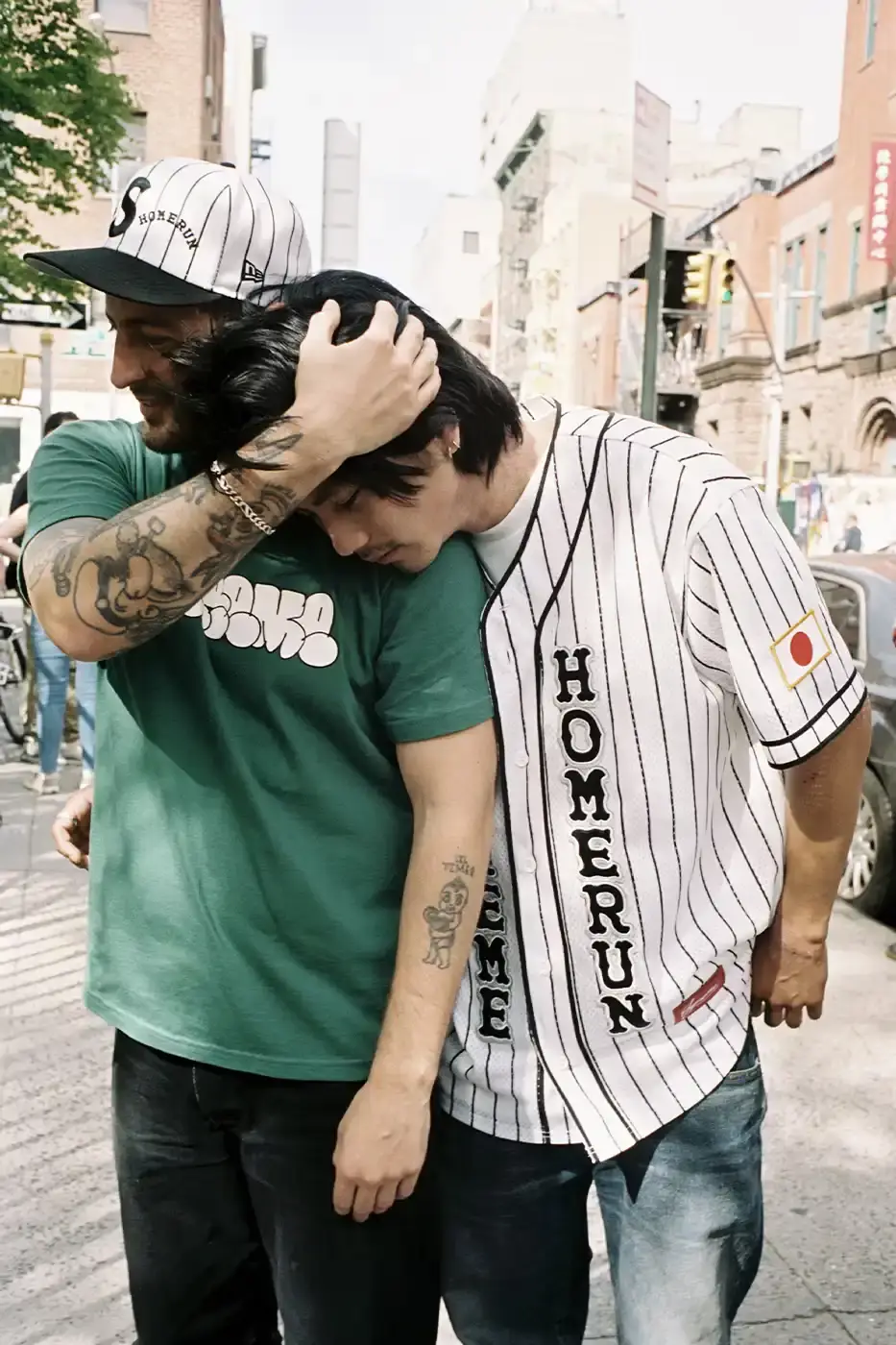 SUPREME PARTNERS WITH HOMERUN FOR BASEBALL-INSPIRED COLLECTION image of the Spring 2025 collaboration between Supreme and Homerun, a brand based in both New York City and Tokyo. The collection features baseball-inspired apparel including varsity jackets in silver and black, baseball jerseys in teal, navy, and pinstriped designs, plus hooded sweatshirts, t-shirts, and New Era caps. All items display co-branding with Homerun's cartoon graphics and "Non Stop" motto. The collection launches May 15 globally and May 17 in Asia through Supreme's website and stores. (image 11 of 14)
