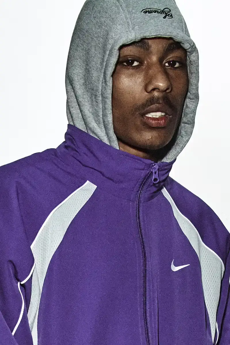 Supreme/Nike Supreme x Nike Spring 2025 Collection featuring black and white Leather Varsity Jackets, purple, yellow and black Track Suits, striped Rugby shirts, Sweater Vests, Hooded Sweatshirts, and accessories including Running Hats and Leather Shoulder Bags. (image 18 of 22)