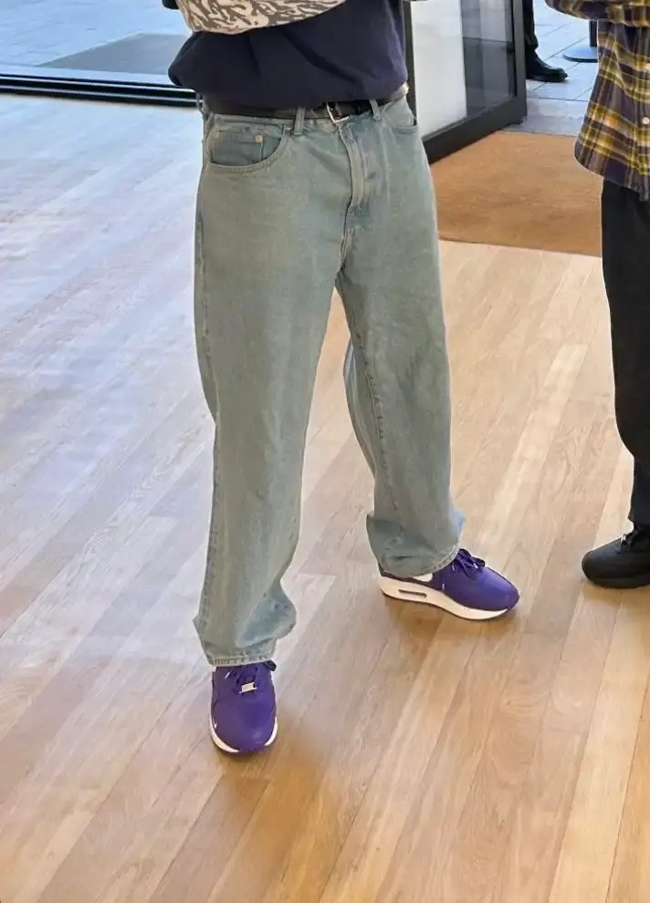 @_clementowusu Close-up photograph of the Supreme x Nike Air Max 1 '87 in Varsity Purple colorway showing white Supreme "World Famous" script on the purple heel counter, white midsole with debossed SUPREME wordmark, and purple upper with white Nike swoosh logo on the side. (image 2 of 2)