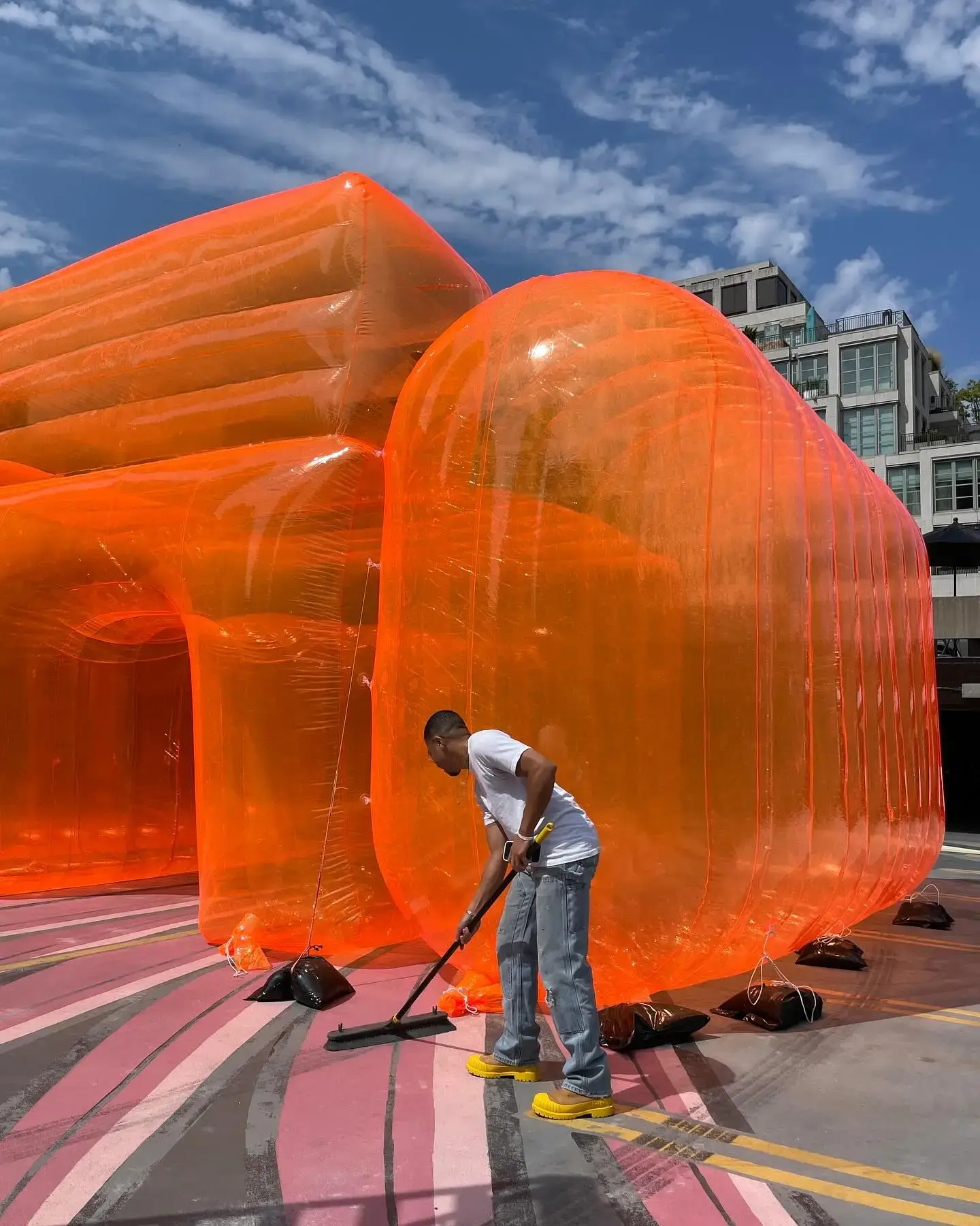 Sean Brown's 'Ego Chair' installation in Toronto: A large, colorful inflatable chair artwork exploring themes of identity and self-perception. The chair stands 6 feet tall, made of transparent PVC with neon pink and blue colors. It's part of Brown's 'Ego' collection at Gallery 44, featuring an interactive element that slowly deflates when sat upon, symbolizing ego deflation. This playful yet thought-provoking piece blends retro aesthetics with modern design, sparking conversations about identity in the digital age