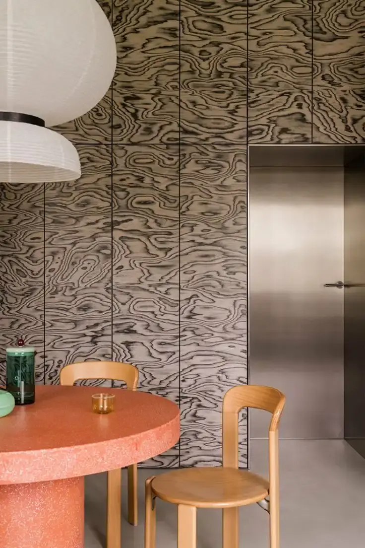 Article wrote by Monica Picchi about the revival of Memphis-style decorative wood veneer, featuring colorful, psychedelic wood grain patterns pioneered by Ettore Sottsass in the 1980s and recently popularized by designers like Sabine Marcelis and Martino Gamper. The technique involves dyeing thin slices of wood to create bold, expressive patterns for furniture and interior design elements.