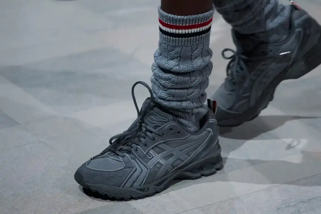 THOM BROWNE ASICS SNEAKER DROPS MARCH 2026 Thom Browne partnered with ASICS to release a redesigned GEL-KAYANO 14 sneaker featuring grey suede, mesh construction, and the designer's tri-color flag detail. The collection launches globally on March 2, 2026.