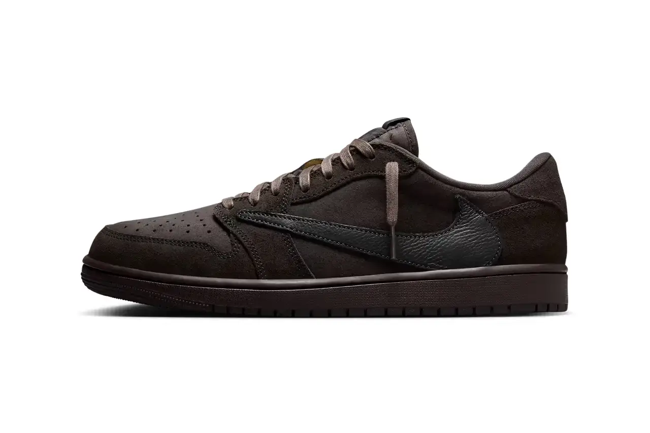 Nike A detailed product shot of the Travis Scott x Air Jordan 1 Low OG "Dark Mocha" sneaker. The shoe features a dark mocha brown leather upper with black overlays, a distinctive reversed lateral Swoosh in tumbled leather, and Cactus Jack branding on the medial side. The sneaker sits against a neutral background, showcasing its intricate design details and color blocking.