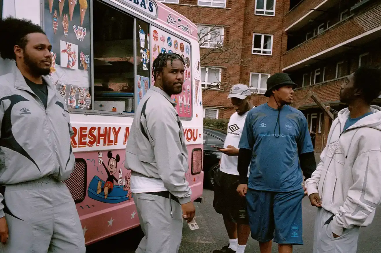 SOUTH LONDON'S FINEST: UMBRO TEAMS UP WITH BOILER ROOM AGAIN image of Umbro's third collaboration with Boiler Room, featuring a clothing collection modeled by UK artists from South London. The collection includes grey tracksuits with black accents, co-branded t-shirts, football jerseys, and hoodies. All items photographed by Simon Wheatley in Lewisham and will be available from both brands on May 15. (image 4 of 7)