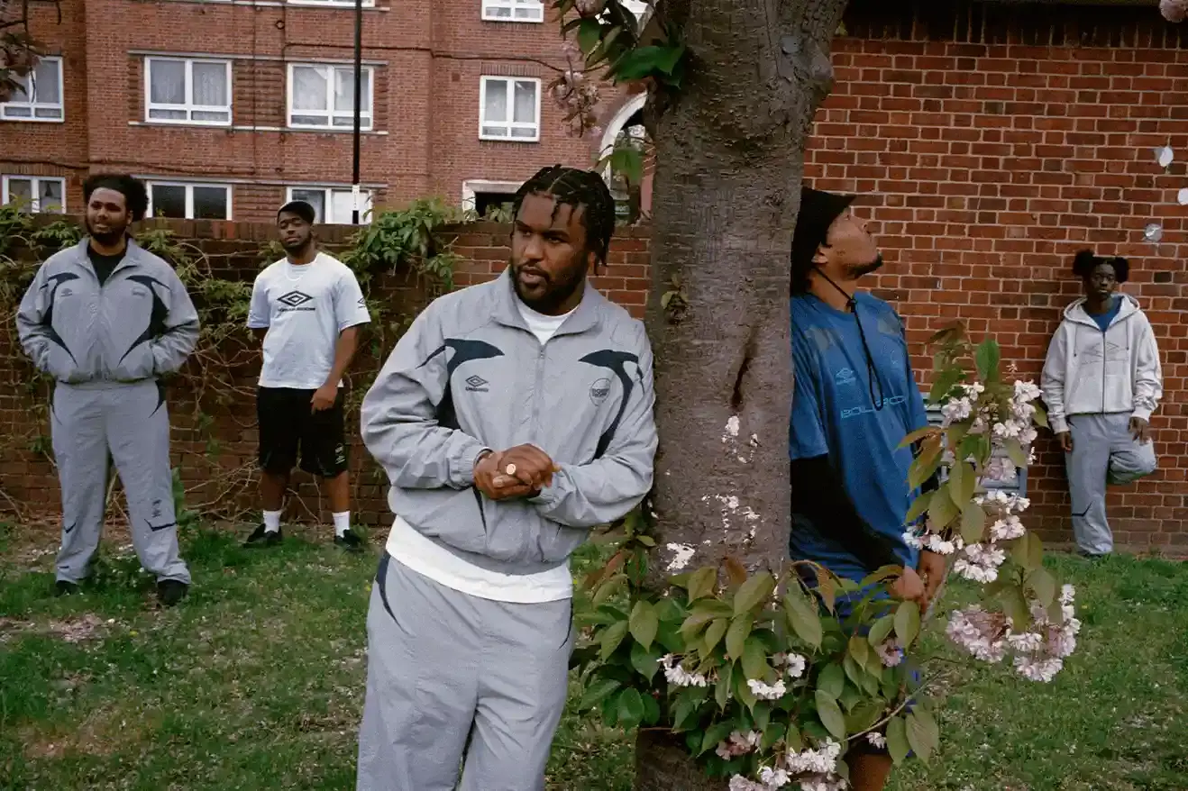 SOUTH LONDON'S FINEST: UMBRO TEAMS UP WITH BOILER ROOM AGAIN image of Umbro's third collaboration with Boiler Room, featuring a clothing collection modeled by UK artists from South London. The collection includes grey tracksuits with black accents, co-branded t-shirts, football jerseys, and hoodies. All items photographed by Simon Wheatley in Lewisham and will be available from both brands on May 15. (image 6 of 7)