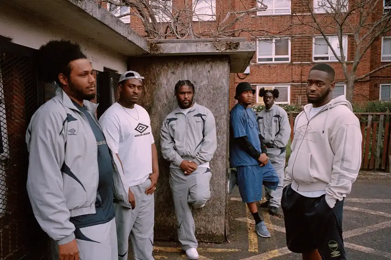 SOUTH LONDON'S FINEST: UMBRO TEAMS UP WITH BOILER ROOM AGAIN image of Umbro's third collaboration with Boiler Room, featuring a clothing collection modeled by UK artists from South London. The collection includes grey tracksuits with black accents, co-branded t-shirts, football jerseys, and hoodies. All items photographed by Simon Wheatley in Lewisham and will be available from both brands on May 15. (image 2 of 7)