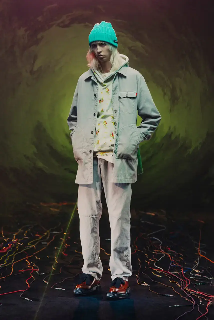 UNDERCOVER Fashion runway image featuring models wearing black tailoring and graphic prints, with neon lighting and monster illustrations by Josep Baqué, representing UNDERCOVER's FW25 collection exploring punk and musical subcultures. (image 5 of 20)