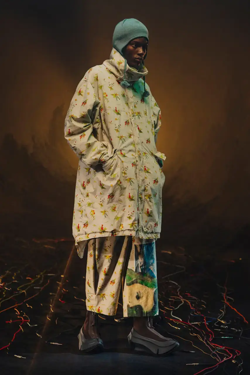 UNDERCOVER Fashion runway image featuring models wearing black tailoring and graphic prints, with neon lighting and monster illustrations by Josep Baqué, representing UNDERCOVER's FW25 collection exploring punk and musical subcultures. (image 4 of 20)