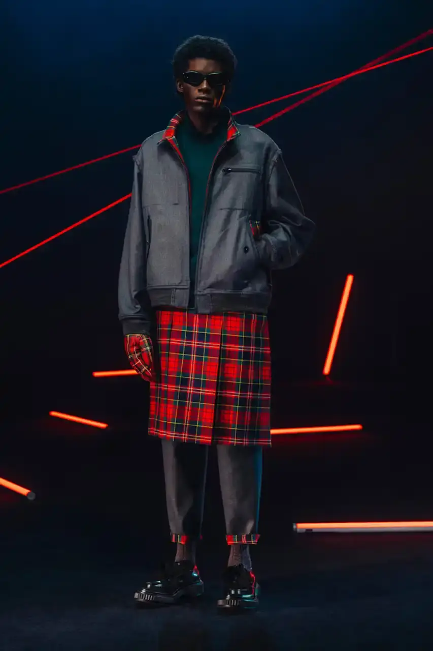 UNDERCOVER Fashion runway image featuring models wearing black tailoring and graphic prints, with neon lighting and monster illustrations by Josep Baqué, representing UNDERCOVER's FW25 collection exploring punk and musical subcultures. (image 2 of 20)