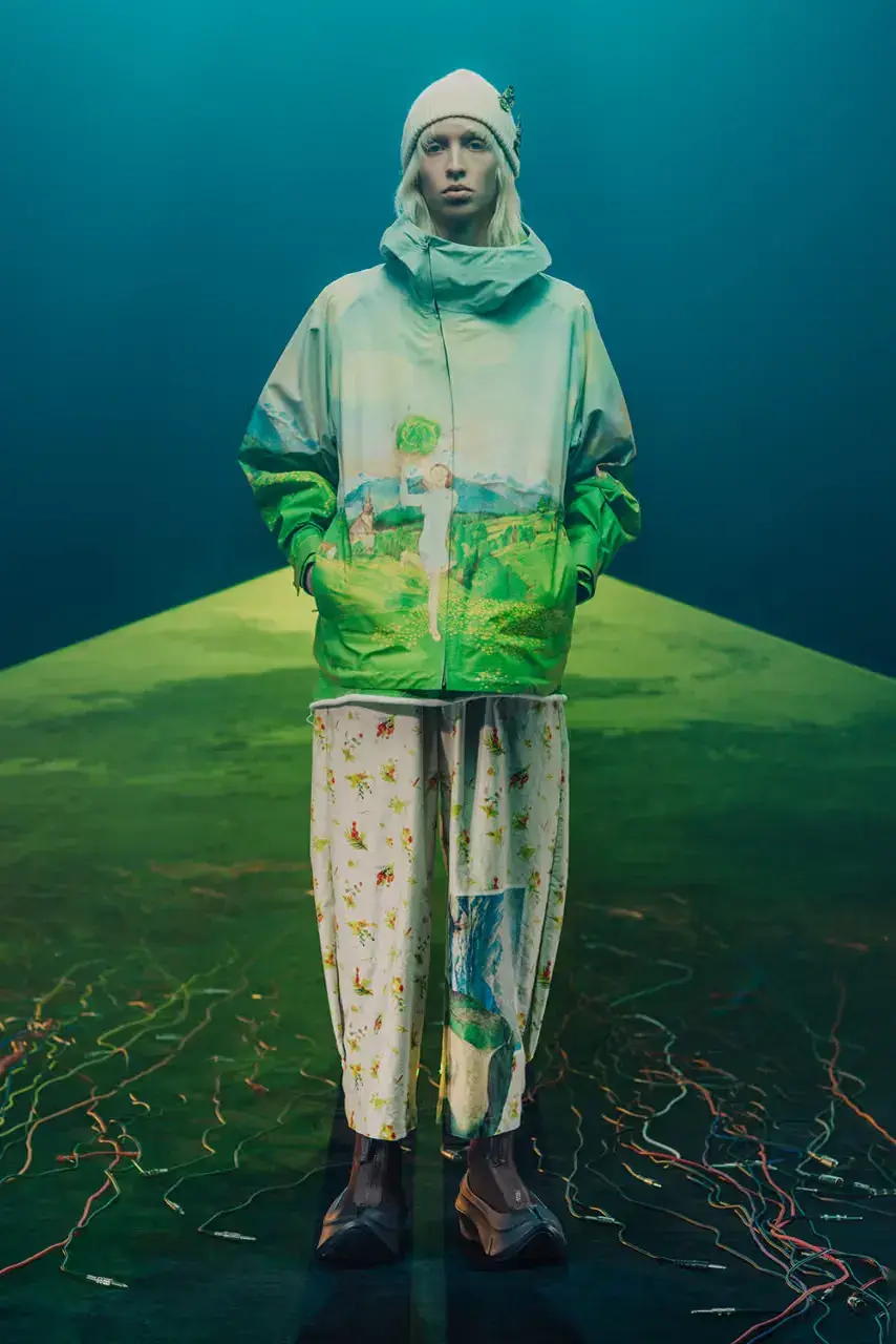 UNDERCOVER Fashion runway image featuring models wearing black tailoring and graphic prints, with neon lighting and monster illustrations by Josep Baqué, representing UNDERCOVER's FW25 collection exploring punk and musical subcultures. (image 6 of 20)