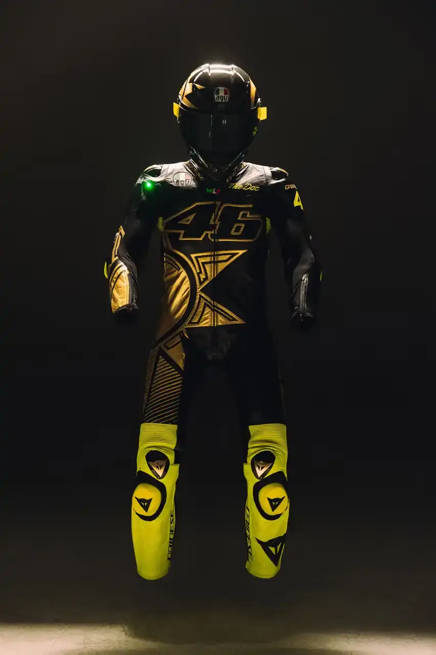 Dainese Dainese's Soleluna Vale46 Anniversary Kit displaying a black racing suit and helmet with yellow accents and gold leaf details, positioned in a glass display case. The gear features Valentino Rossi's signature number 46. (image 2 of 11)