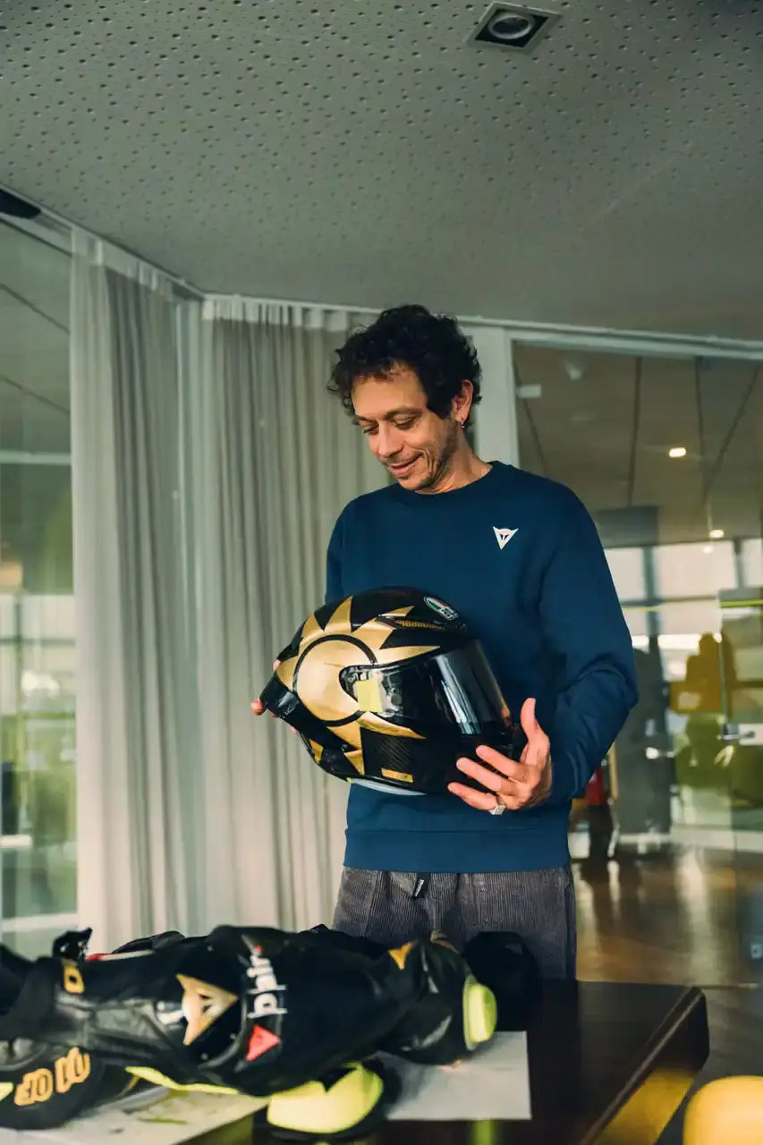 Dainese Dainese's Soleluna Vale46 Anniversary Kit displaying a black racing suit and helmet with yellow accents and gold leaf details, positioned in a glass display case. The gear features Valentino Rossi's signature number 46. (image 3 of 11)