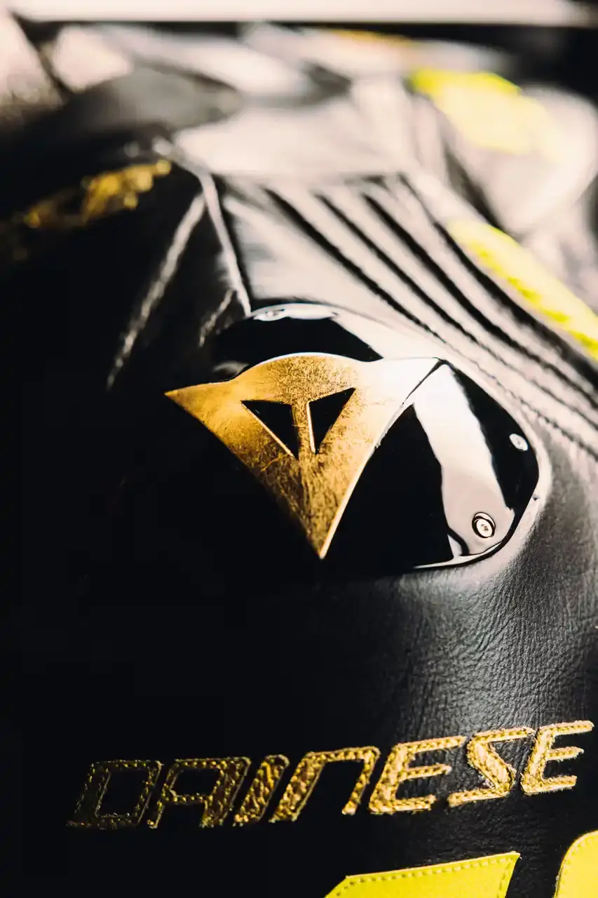 Dainese Dainese's Soleluna Vale46 Anniversary Kit displaying a black racing suit and helmet with yellow accents and gold leaf details, positioned in a glass display case. The gear features Valentino Rossi's signature number 46. (image 10 of 11)