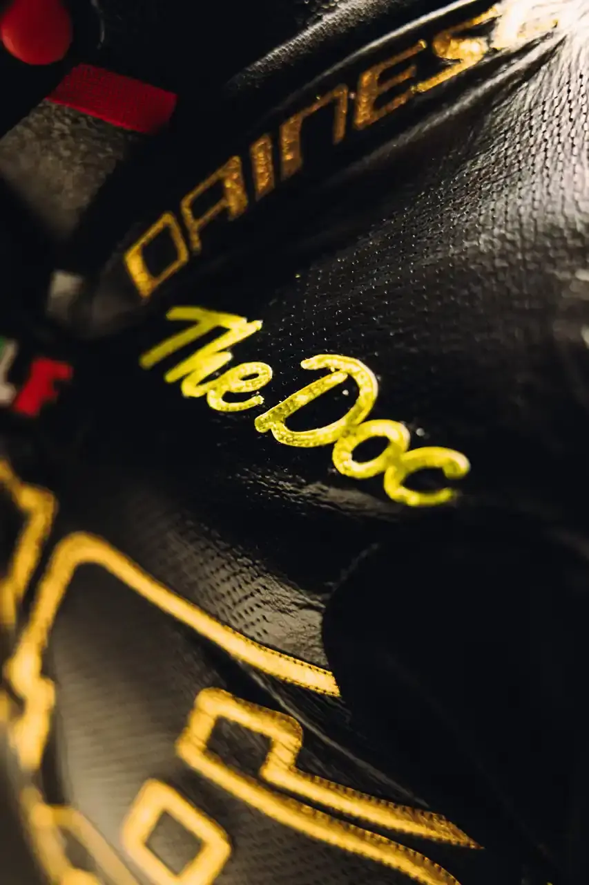 Dainese Dainese's Soleluna Vale46 Anniversary Kit displaying a black racing suit and helmet with yellow accents and gold leaf details, positioned in a glass display case. The gear features Valentino Rossi's signature number 46. (image 11 of 11)