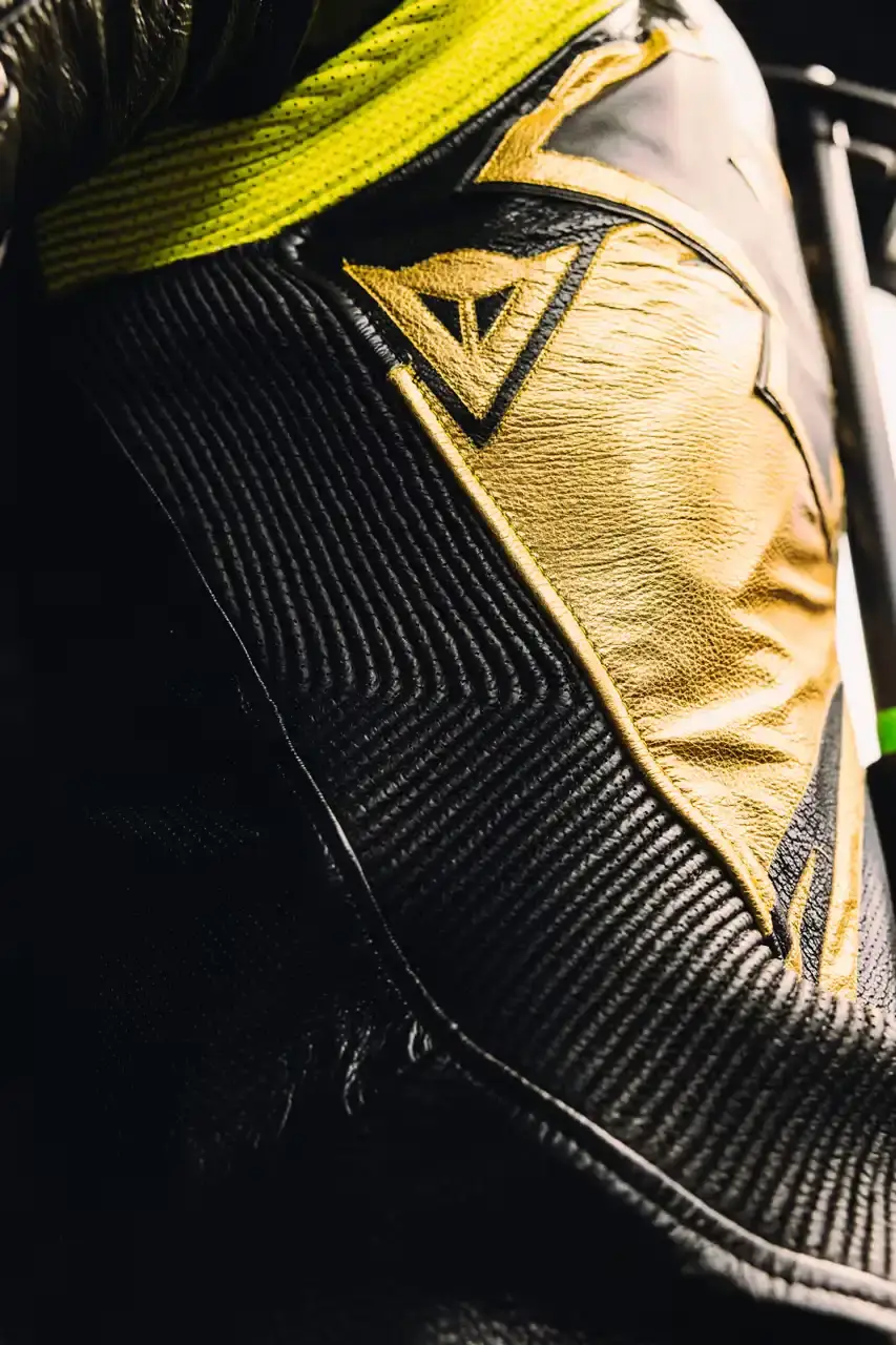 Dainese Dainese's Soleluna Vale46 Anniversary Kit displaying a black racing suit and helmet with yellow accents and gold leaf details, positioned in a glass display case. The gear features Valentino Rossi's signature number 46. (image 8 of 11)