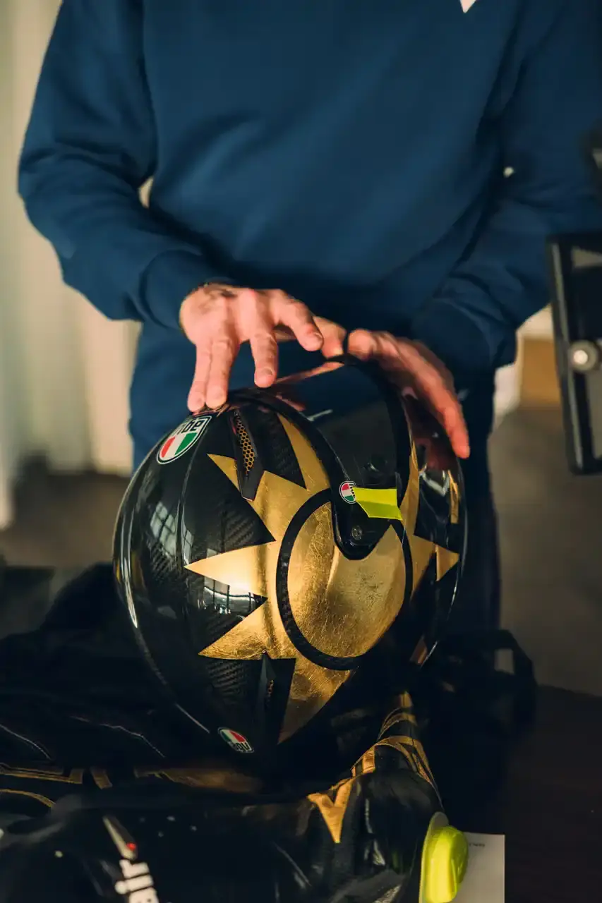 Dainese Dainese's Soleluna Vale46 Anniversary Kit displaying a black racing suit and helmet with yellow accents and gold leaf details, positioned in a glass display case. The gear features Valentino Rossi's signature number 46. (image 7 of 11)