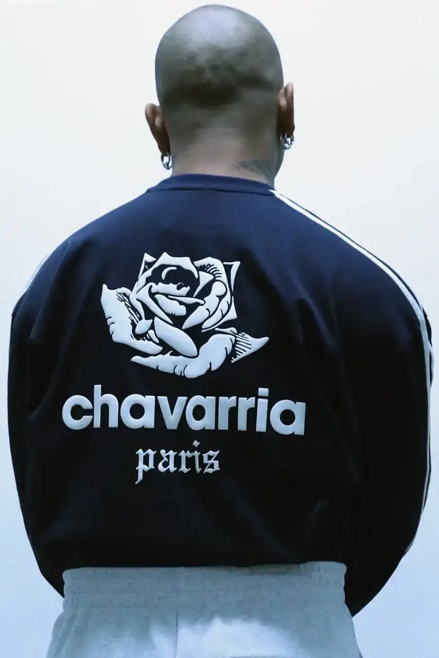 adidas Originals/Willy Chavarria Image shows a vintage Chevrolet Impala parked on a Parisian street, displaying Willy Chavarria x adidas Originals limited-edition apparel and footwear collection, featuring navy t-shirts, hoodies, and sneakers with rose motifs and collaborative branding. (image 5 of 7)