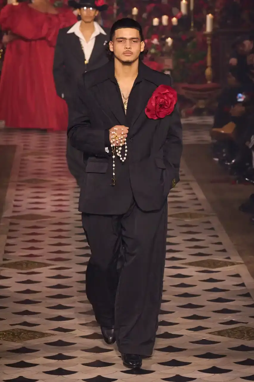 Daniele Oberrauch/Gorunway.com/Vogue Runway A diverse runway scene featuring models of various ages, body types, and backgrounds wearing Willy Chavarria's Fall 2025 "Tarantula" collection. The designs showcase rose-adorned blazers, Western-inspired hats, and a rich color palette of gold, blue, crimson, and plum against the backdrop of The American Cathedral in Paris. (image 3 of 15)