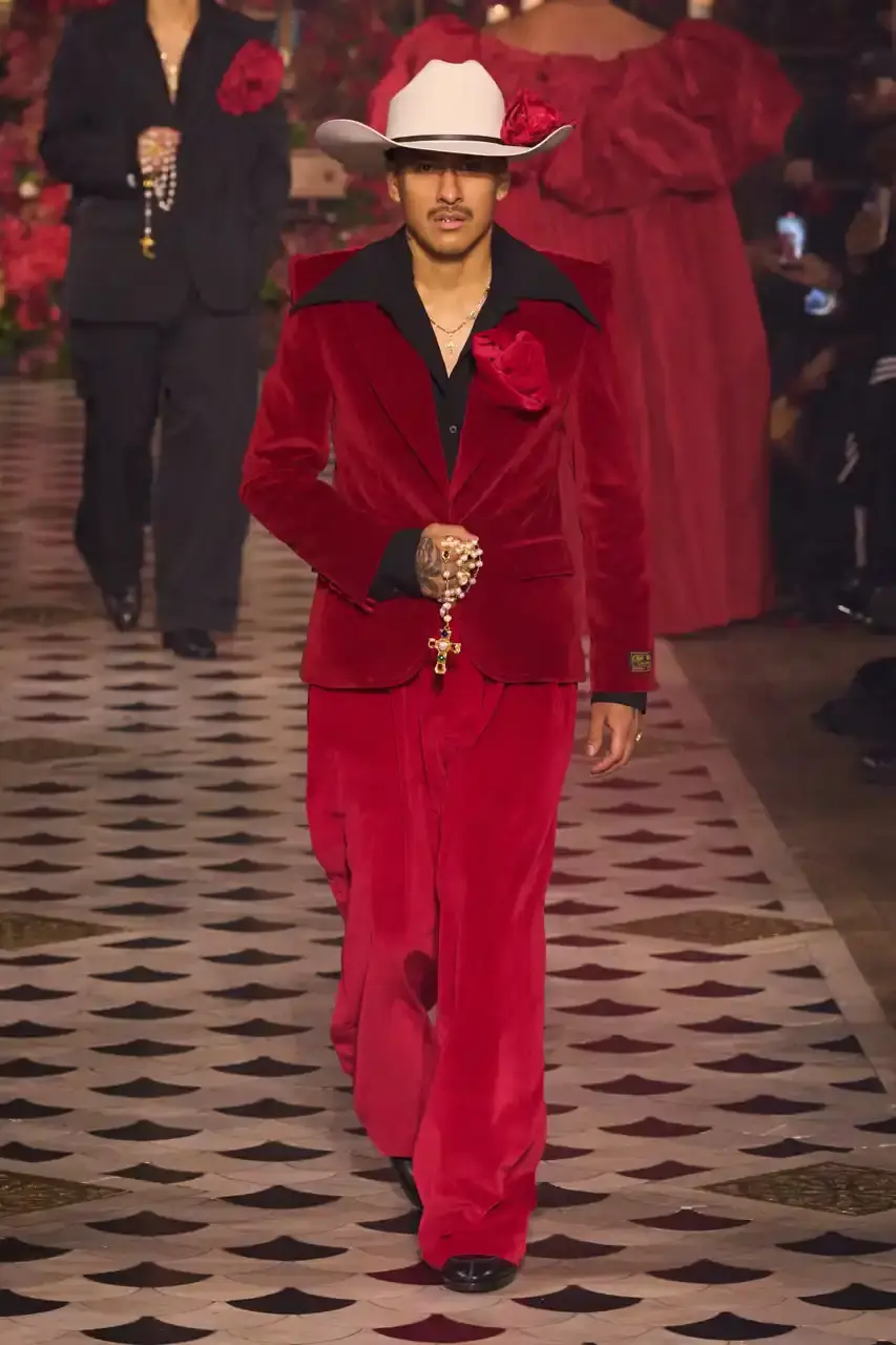 Daniele Oberrauch/Gorunway.com/Vogue Runway A diverse runway scene featuring models of various ages, body types, and backgrounds wearing Willy Chavarria's Fall 2025 "Tarantula" collection. The designs showcase rose-adorned blazers, Western-inspired hats, and a rich color palette of gold, blue, crimson, and plum against the backdrop of The American Cathedral in Paris. (image 2 of 15)