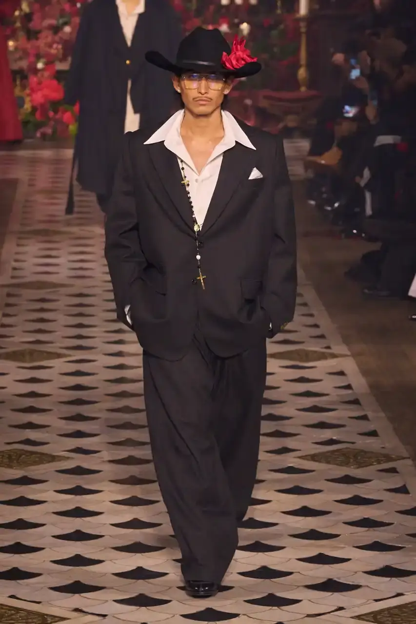 Daniele Oberrauch/Gorunway.com/Vogue Runway A diverse runway scene featuring models of various ages, body types, and backgrounds wearing Willy Chavarria's Fall 2025 "Tarantula" collection. The designs showcase rose-adorned blazers, Western-inspired hats, and a rich color palette of gold, blue, crimson, and plum against the backdrop of The American Cathedral in Paris. (image 5 of 15)