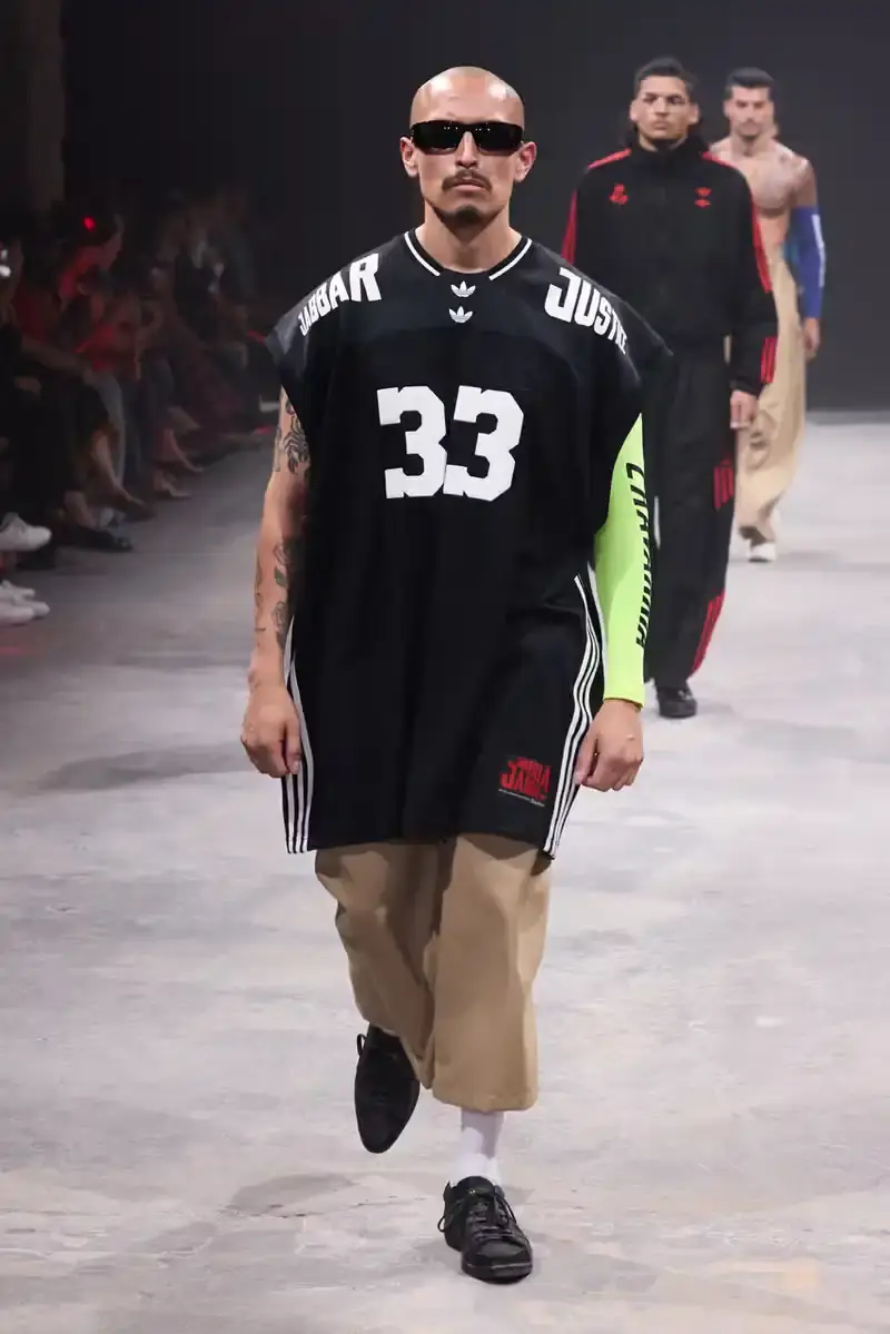 WILLY CHAVARRIA SS25: A SARTORIAL ODE TO THE AMERICAN DREAM Athletic model showcasing Willy Chavarria x adidas collaboration: avant-garde quarter-zip jacket with prominent Three Stripes logo (image 13 of 15)