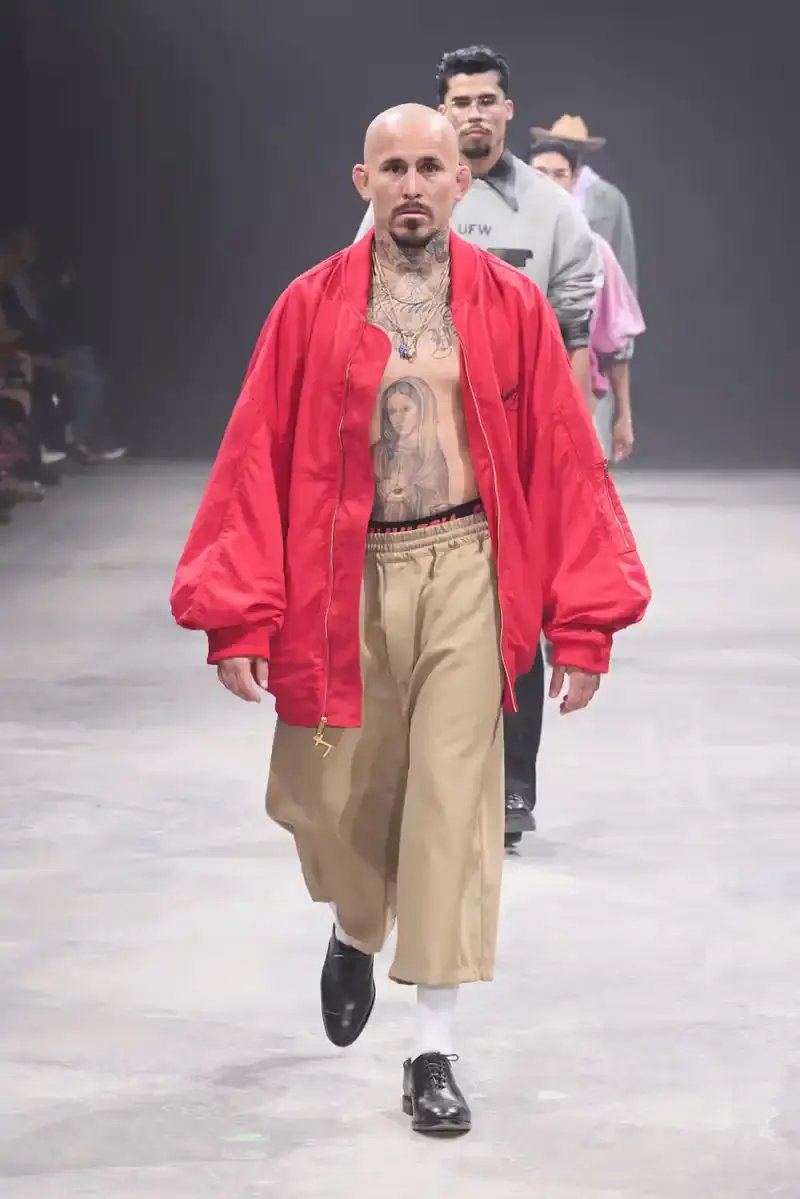 WILLY CHAVARRIA SS25: A SARTORIAL ODE TO THE AMERICAN DREAM Models walk the runway at Willy Chavarria's SS25 'América' show, wearing dramatic workwear-inspired designs against an industrial backdrop (image 9 of 15)
