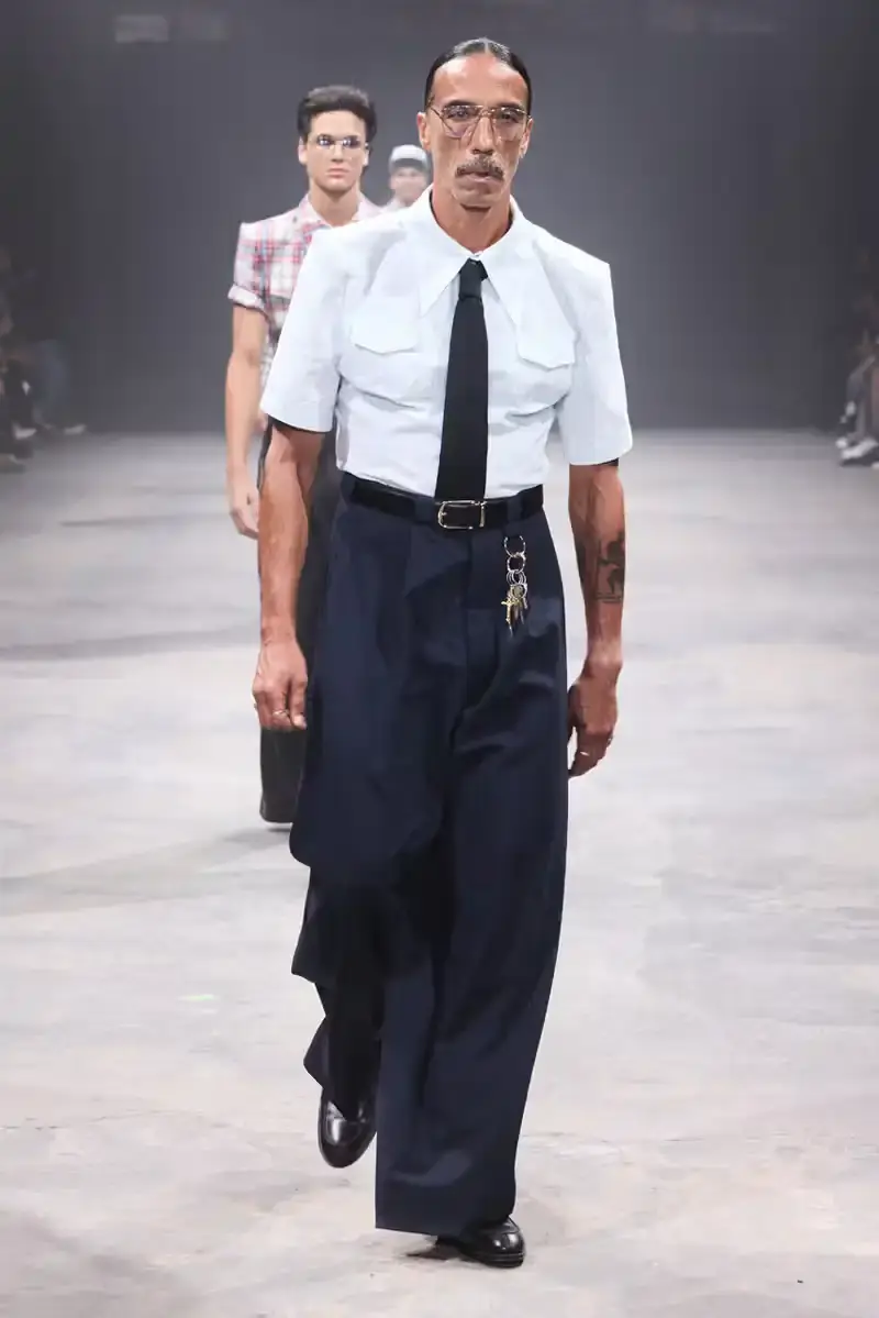 WILLY CHAVARRIA SS25: A SARTORIAL ODE TO THE AMERICAN DREAM Models walk the runway at Willy Chavarria's SS25 'América' show, wearing dramatic workwear-inspired designs against an industrial backdrop (image 8 of 15)