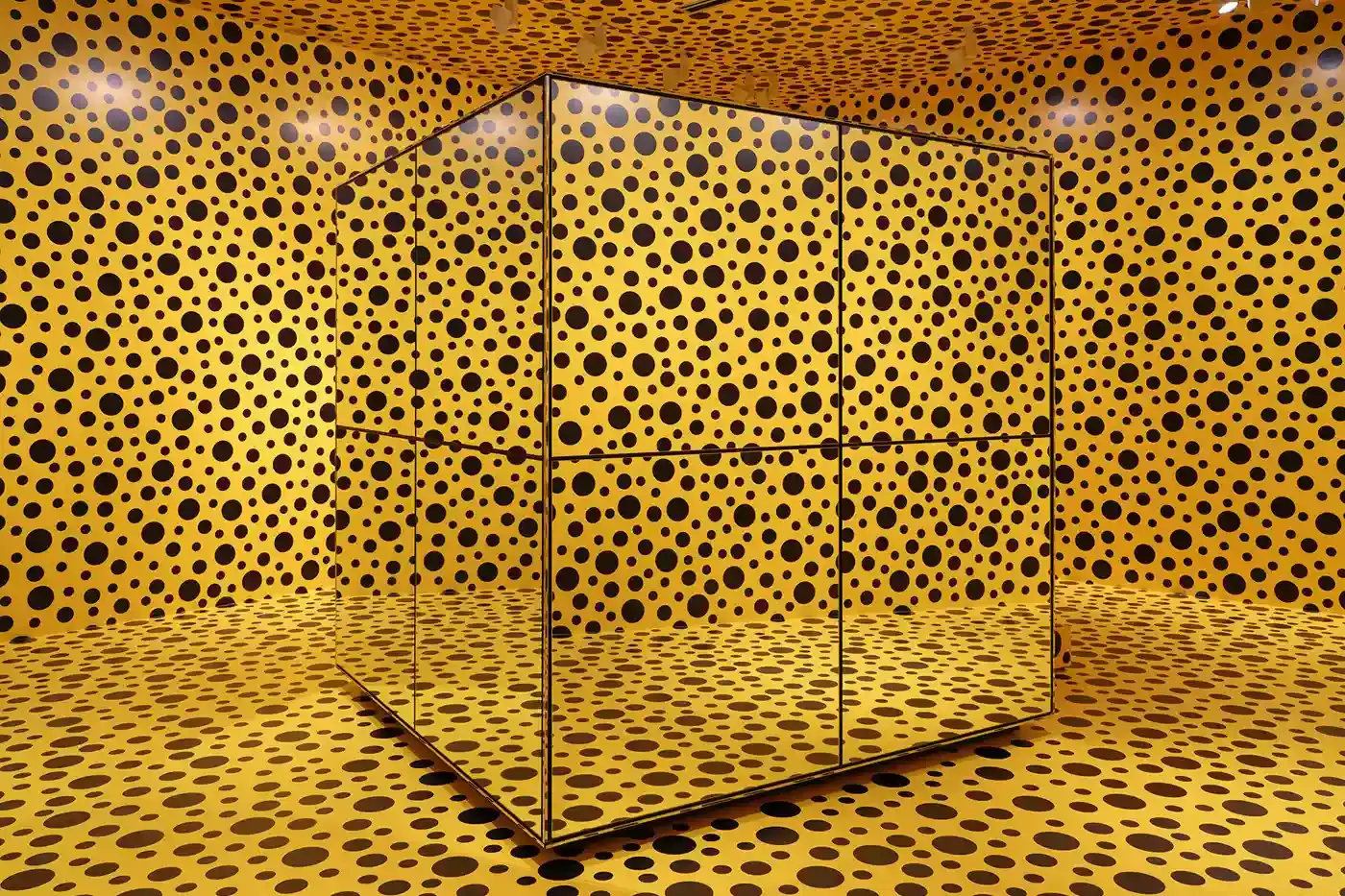 Sean Fennessy/Yayoi Kusama A photograph of Yayoi Kusama's immersive infinity mirrored room, featuring reflective surfaces creating a kaleidoscopic environment of endless light and geometric patterns. Polka-dotted sculptures and vibrant yellow and black elements are visible, representing the artist's signature visual style. (image 10 of 13)