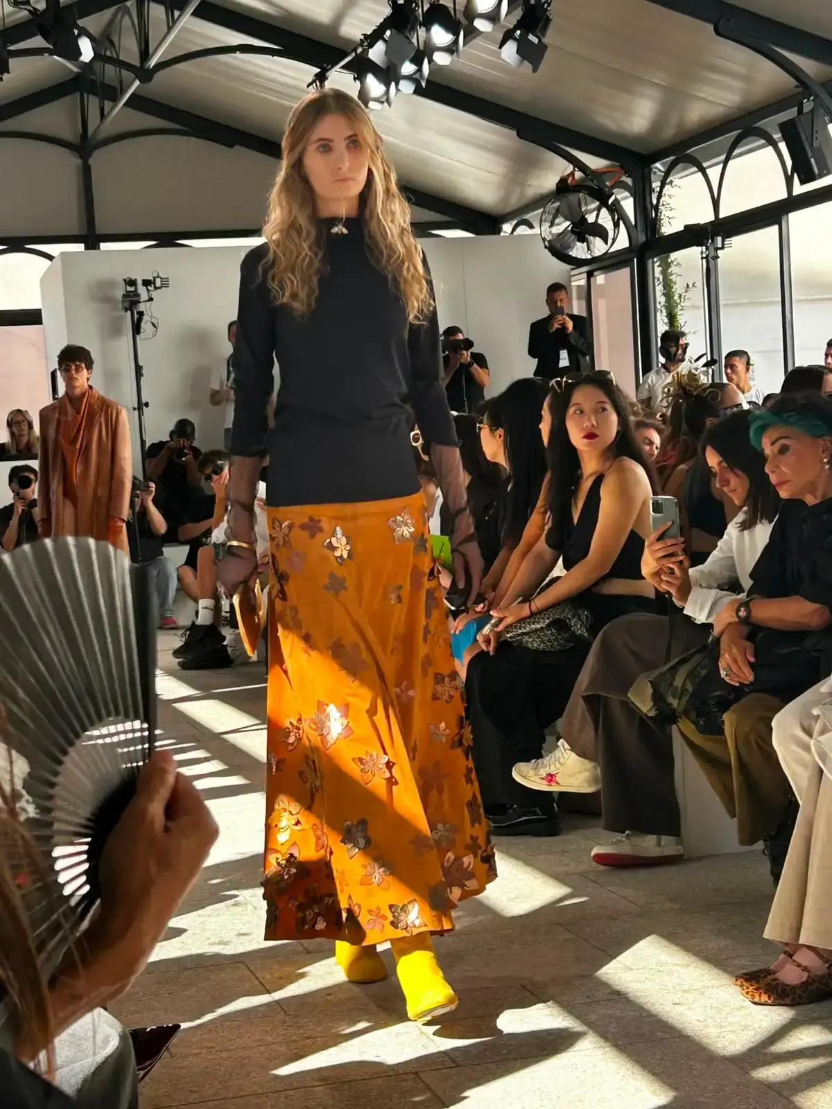 YEZAEL "VERITÀ" COLLECTION BY ANGELO CRUCIANI image of Marche-born designer Angelo Cruciani's "Verità" collection for Yezael presented at Fashion Week 2026. The text describes tailored suits with wide-leg trousers, 3D floral appliqués, an ochre-yellow coat, a pastel-blue Rococo-inspired suit, and contrasting textures combining leather and pearls. Key quotes and philosophical reflections explore fashion, consumerism, nature, and personal identity. (image 2 of 12)