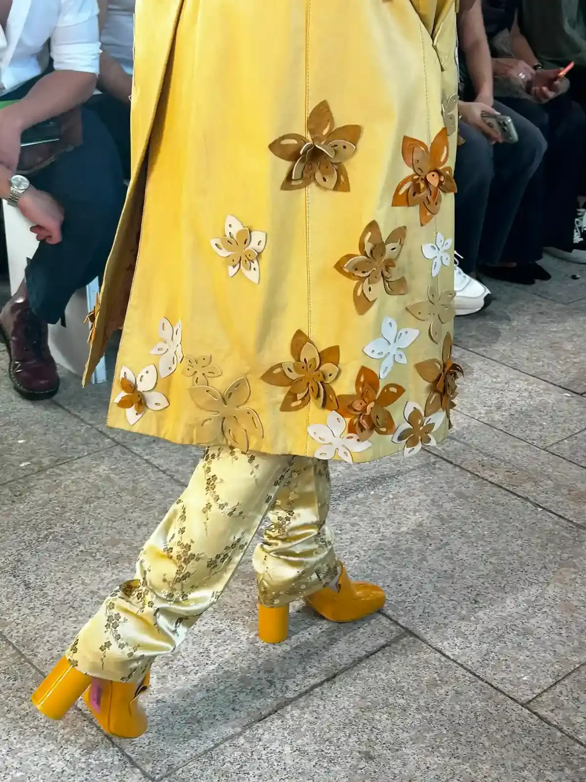 YEZAEL "VERITÀ" COLLECTION BY ANGELO CRUCIANI image of Marche-born designer Angelo Cruciani's "Verità" collection for Yezael presented at Fashion Week 2026. The text describes tailored suits with wide-leg trousers, 3D floral appliqués, an ochre-yellow coat, a pastel-blue Rococo-inspired suit, and contrasting textures combining leather and pearls. Key quotes and philosophical reflections explore fashion, consumerism, nature, and personal identity. (image 7 of 12)