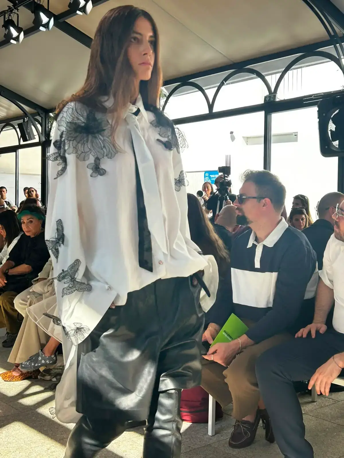YEZAEL "VERITÀ" COLLECTION BY ANGELO CRUCIANI image of Marche-born designer Angelo Cruciani's "Verità" collection for Yezael presented at Fashion Week 2026. The text describes tailored suits with wide-leg trousers, 3D floral appliqués, an ochre-yellow coat, a pastel-blue Rococo-inspired suit, and contrasting textures combining leather and pearls. Key quotes and philosophical reflections explore fashion, consumerism, nature, and personal identity. (image 8 of 12)