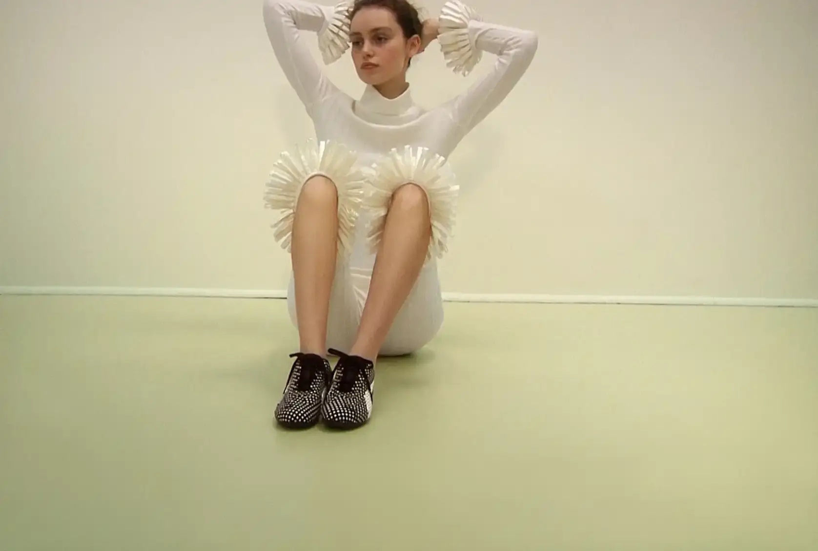 ZALANDO AND SUPER YAYA REWORK THE PUMA SPEEDCAT Photograph of model Alek Wek sitting on the floor wearing a white outfit with ruffled knee details and black and white patterned sneakers.