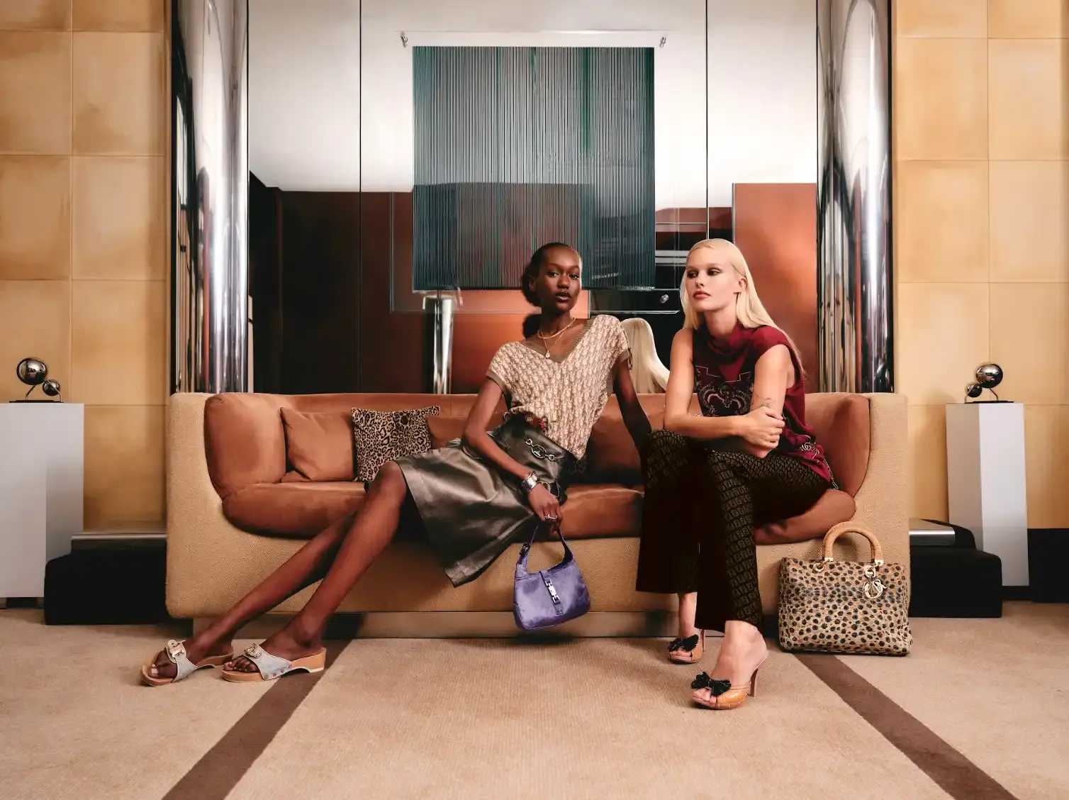 ZALANDO PARTNERS WITH VESTIAIRE COLLECTIVE FOR LUXURY Two women sit on a sofa wearing designer clothing and accessories including leather skirts and animal print bags in a modern interior setting.
